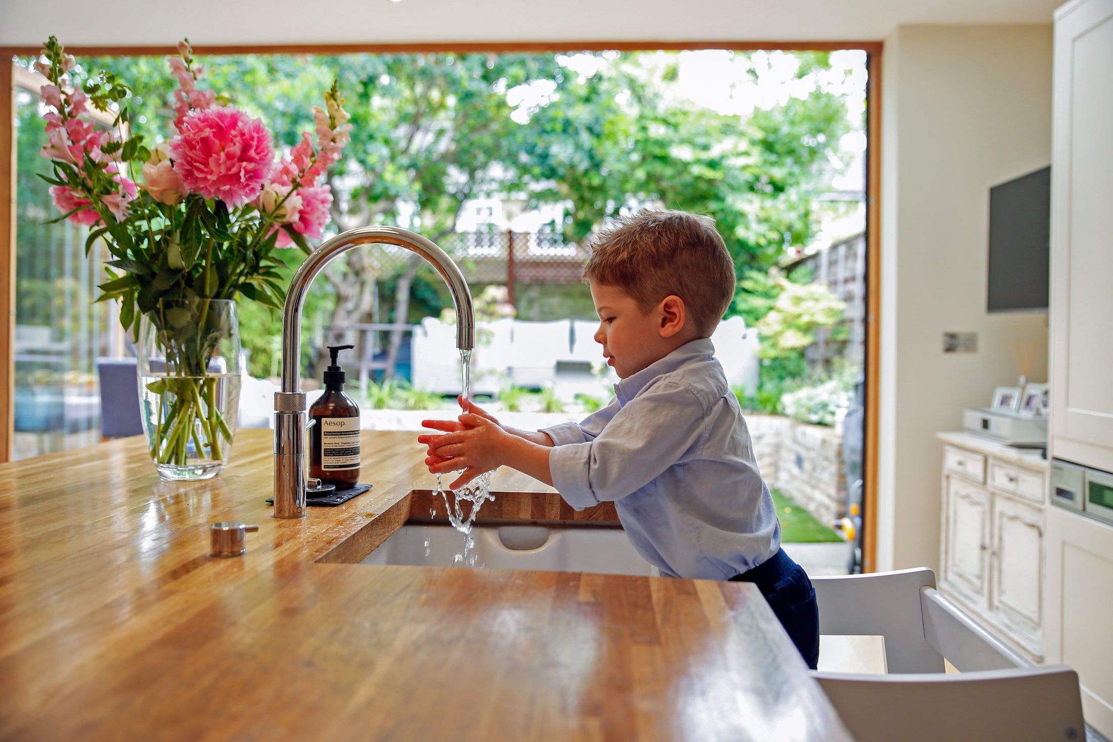 Child washing hands in Toddler Tower. Supporting child development and independent hygiene during COVID-19 with kitchen helper.